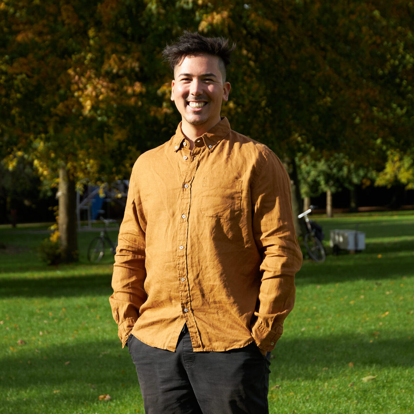 Joey in a gold shirt smiling at the camera, against an autumn forest background